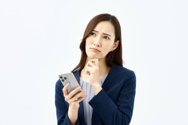 スマホを持ち考える女性